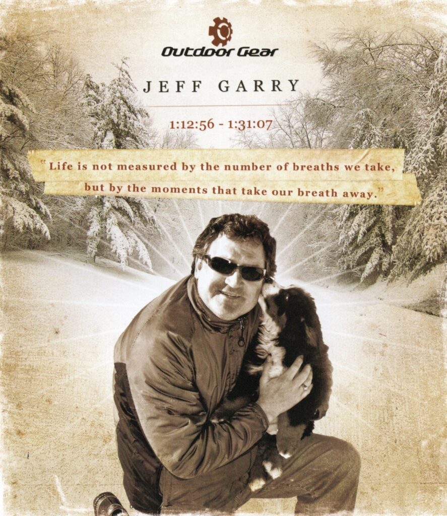 A memorial for Jeff Garry, pictured holding a dog in a snowy, forested area. The graphic reads: Outdoor Gear Jeff Garry 1:12:56 - 1:31:07. "Life is not measured by the number of breaths we take, but by the moments that take our breath away."