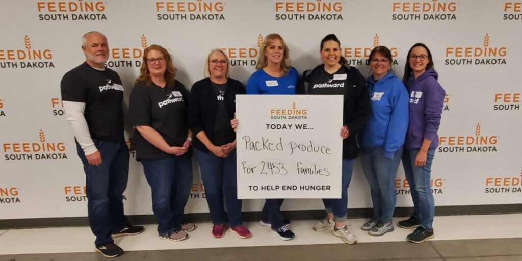 Pathward employees at Feeding South Dakota with a sign saying they packed produce for 2,453 families.
